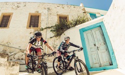 Zwei Mountainbiker fahren eine Treppe in einem typisch griechisch anmutenden Ort hinunter.