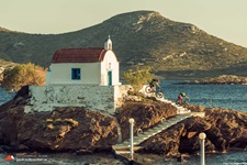 Zwei Mountainbiker auf den Stufen der vom Meer umgebenen Kirche Agios Isidoros.