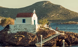 Zwei Mountainbiker auf den Stufen der vom Meer umgebenen Kirche Agios Isidoros.