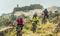 Drei Mountainbiker auf Patmos vor der Kulisse des Klosters des Heiligen Johannes.