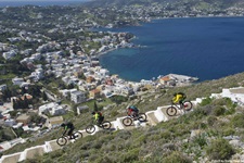 Vier Mountainbiker fahren auf der Insel Leros eine asphaltierte, parallel zur Küste verlaufende Treppe hinunter.