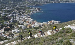 Vier Mountainbiker fahren auf der Insel Leros eine asphaltierte, parallel zur Küste verlaufende Treppe hinunter.