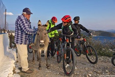 Eine Gruppe Mountainbiker auf Patmos streichelt einen Esel und plaudert mit dessen Besitzer.