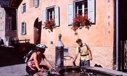 Ein Radlerpärchen macht an einem Brunnen in einem Engadiner Dorf Pause.