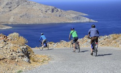 Drei Radfahrer radeln auf einer Straße auf der griechischen Insel Patmos entlang - im Hintergrund ist das tiefblaue Meer zu sehen
