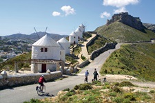 Viier Radler radeln auf einem Weg an den fünf Windmühlen vor der Burg auf der Insel Leros in der Griechischen Ägäis vorbei