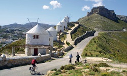 Viier Radler radeln auf einem Weg an den fünf Windmühlen vor der Burg auf der Insel Leros in der Griechischen Ägäis vorbei