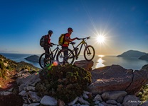 Zwei Mountainbiker beobachten den Sonnenaufgang über der Ägäis.