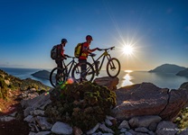 Zwei Mountainbiker beobachten den Sonnenaufgang über der Ägäis.