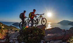 Zwei Mountainbiker beobachten den Sonnenaufgang über der Ägäis.