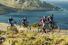 Vier Mountainbiker radeln an einer Steilküste einen breiten Trail entlang