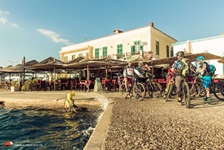Eine Gruppe Mountainbiker legt eine Pause an einem Hafen in der Südlichen Ägäis ein, hinter ihnen ist ein Café zu sehen