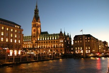 Blick über die Elbe zum nächtlich beleuchteten Rathaus und einigen Geschäften in Hamburg