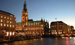 Blick über die Elbe zum nächtlich beleuchteten Rathaus und einigen Geschäften in Hamburg