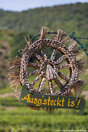 Ein aus Stroh gefertigtes Rad als Heurigenschild und einem weiteren Schild mit der Aufschrift "Ausg´steckt is´!" in Niederösterreich