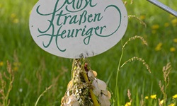 Ein uriges Heurigenschild in Österreich vor einer gelb blühenden Wiese.