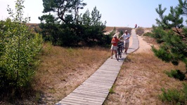 Ein Radlerpärchen schiebt seine Räder über einen Holzsteg durch die Dünenlandschaft der Kurischen Nehrung.