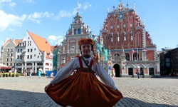 Ein kleines Mädchen in Tracht tanzt vor dem Rathaus von Riga.