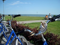 Einige Radler haben ihre Räder abgestellt und machen auf einer Bank unweit der Ostseeküste Pause.