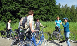 Eine Radlergruppe steigt nach einer Pause wieder auf ihre Räder und lauscht dabei ihrer Reiseleiterin.