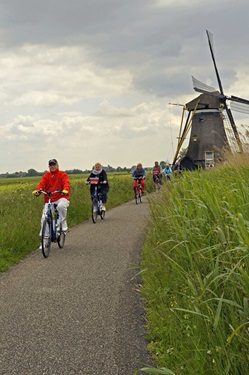 Radfahrer fahren auf einem geteerten Radweg von einer der typischen Mühlen in Holland weg