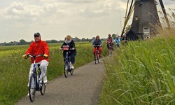 Radfahrer fahren auf einem geteerten Radweg von einer der typischen Mühlen in Holland weg
