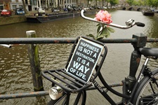 Ein altes Fahrrad mit einer Blume auf dem Lenker und einem Schild mit der Aufschrift "HAPPINIES IST NOT A DESTINATION, IT IS A WAY OF LIFE" auf einer Brücke über einen Fluss in Holland