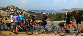 Eine Radlergruppe genießt ihre Pause vor der Kulisse einer traumhaften Bucht an der Costa Smeralda.