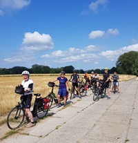 Eine Radlergruppe posiert auf einem mit Betonplatten angelegten Weg zwischen Feldern auf der Insel Rügen für ein Foto
