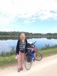 Eine Frau steht auf dem Donau-Radweg neben ihrem Fahrrad, dahinter ist die Donau zu sehen