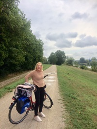 Eine Frau hält ihr Fahrrad auf dem Donauradweg und blickt in die Kamera