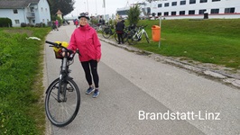 Eine Radfahrerin steht neben ihrem Fahrrad, im Hintergrund das Schiff MS Carissima in Brandstatt-Linz