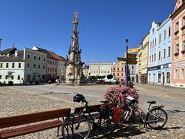 Zwei Fahrräder stehen an an Bänken und einem Wegweiser des Marktplatzes in Jindřichův Hradec mit Blick auf die Dreifaltigkeitssäule