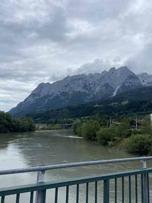 Blick von einer Brücke des Alpe-Adria-Radwegs über einen Fluss zu der einzigartigen Bergkulisse