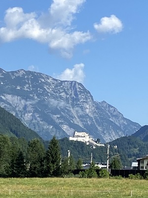 Blick zu einem imposanten Gebäude auf einem kleinen Berg am Alpe-Adria-Radweg und die eindrucksvolle Kulisse eines riesigen Berges