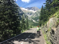 Eine Radlerin schiebt ihr Fahrrad und blickt in die eindrucksvolle Landschaft der Berge auf dem Aare-Radweg