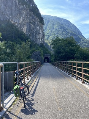 Ein Fahrrad steht vor einem kleinen Tunnel auf einer Brücke auf dem Alpe-Adria-Radweg an einem Geländer