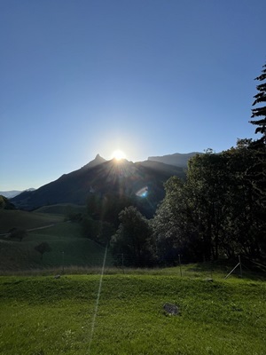 Blick auf die hinter den Alpen aufgehende Sonne auf der Alpenpanorama-Route