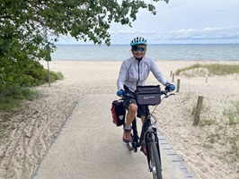 Eine Radfaherin fährt vom Strand der Ostsee weg und lächelt in die Kamera