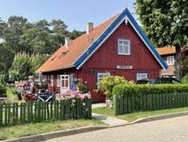 Ein rotes Holzhaus mit blau-weißem Giebel und gepflegtem Garten auf der geführten Radreise "Höhepunkte des Baltikums"