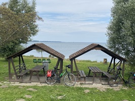 Zwei Fahrräder stehen an einem Picknickplatz mit überdachten Holzbänken und der Ostsee im Hintergrund