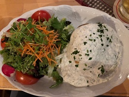 Ofenkartoffel mit Joghurtsoße und einem grünen Salat mit Tomaten und Karottenstreifen auf einem Teller angerichtet