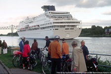 Eine Gruppe Radler blickt auf den Nord-Ostsee-Kanal, auf dem ein Kreuzfahrtschiff fährt