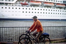 Ein Radfahrer fährt auf dem Radweg entlang des Nord-Ostsee-Kanals, auf dem ein Kreuzfahrtschiff einläuft