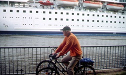 Ein Radfahrer fährt auf dem Radweg entlang des Nord-Ostsee-Kanals, auf dem ein Kreuzfahrtschiff einläuft