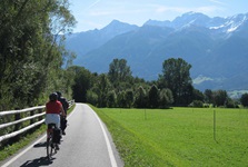 Zwei Radfahrer radeln auf dem Etsch-Radweg mit Blick auf die Alpen