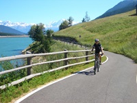 Ein Radfahrer auf dem Etsch-Radweg am Reschensee - im Hintergrund die schneebedeckten Alpengipfel