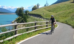 Ein Radfahrer auf dem Etsch-Radweg am Reschensee - im Hintergrund die schneebedeckten Alpengipfel