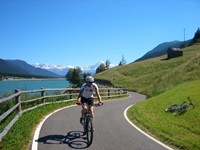 Ein Radfahrer radelt auf dem Etsch-Radweg am Reschensee vorbei - in der Wiese auf der rechten Seite liegt ein Fahrrad