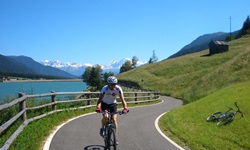 Ein Radfahrer radelt auf dem Etsch-Radweg am Reschensee vorbei - in der Wiese auf der rechten Seite liegt ein Fahrrad
